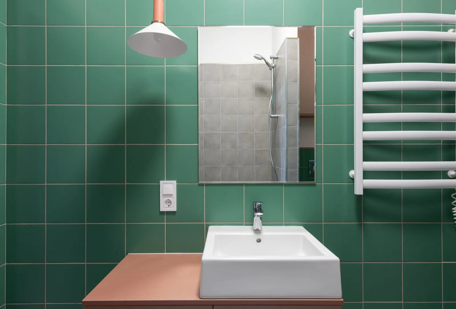 Modern bathroom with green tiled walls and white ceramic sink under mirror reflecting shower designed in minimal style